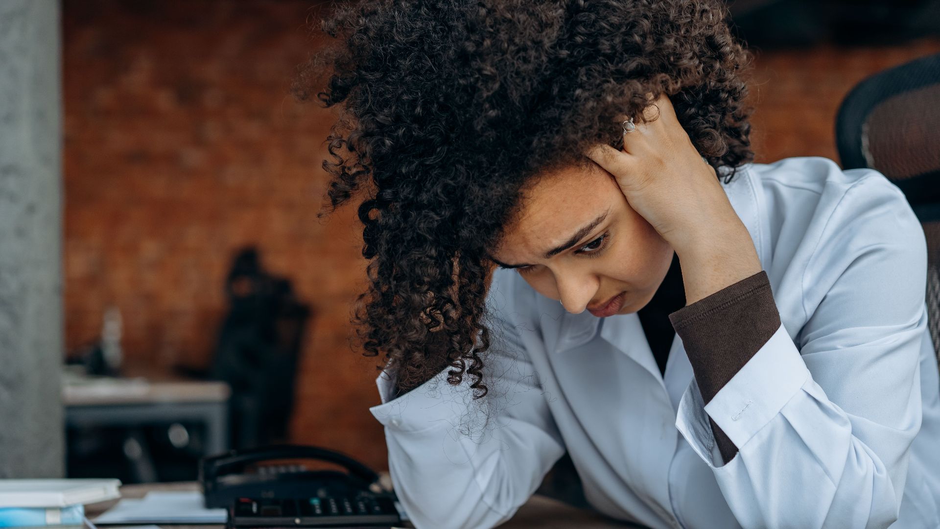 A woman in an office appears stressed while reviewing documents at her desk.