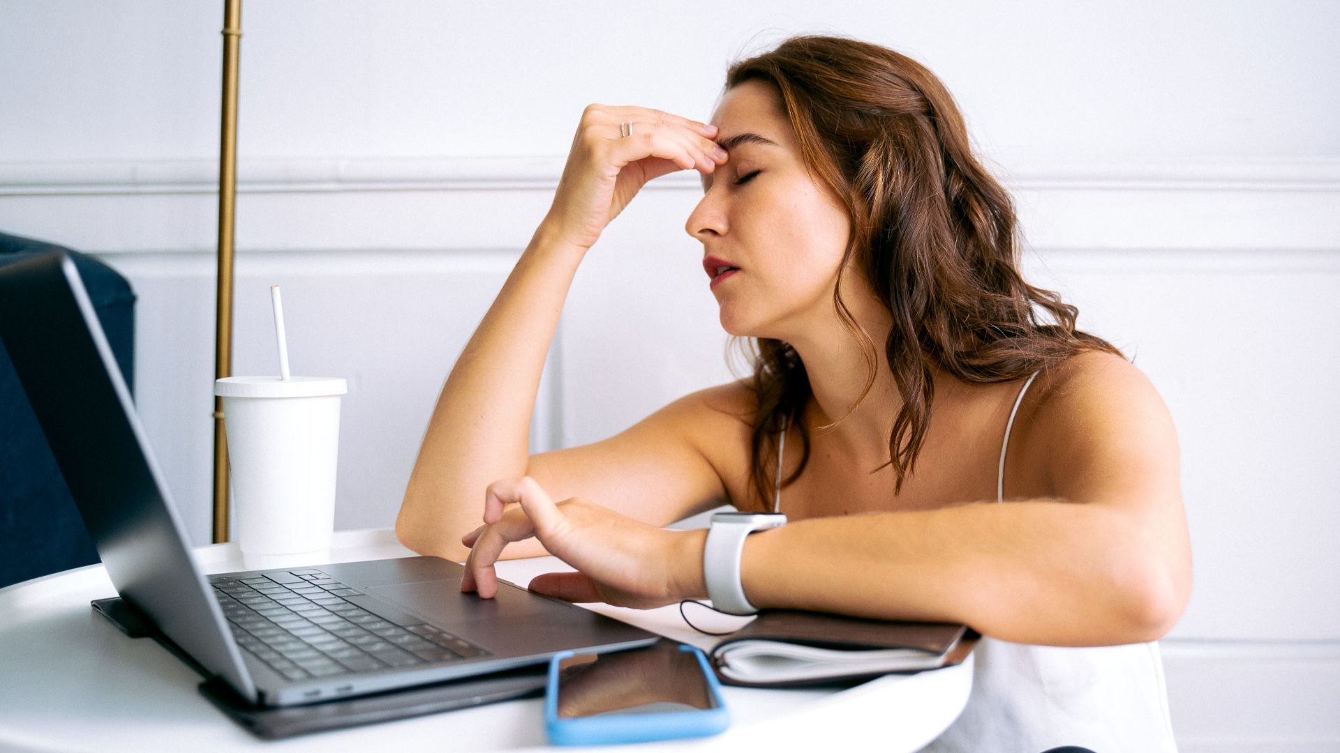 Woman experiencing work fatigue with laptop at a table, indicating stress and tiredness.