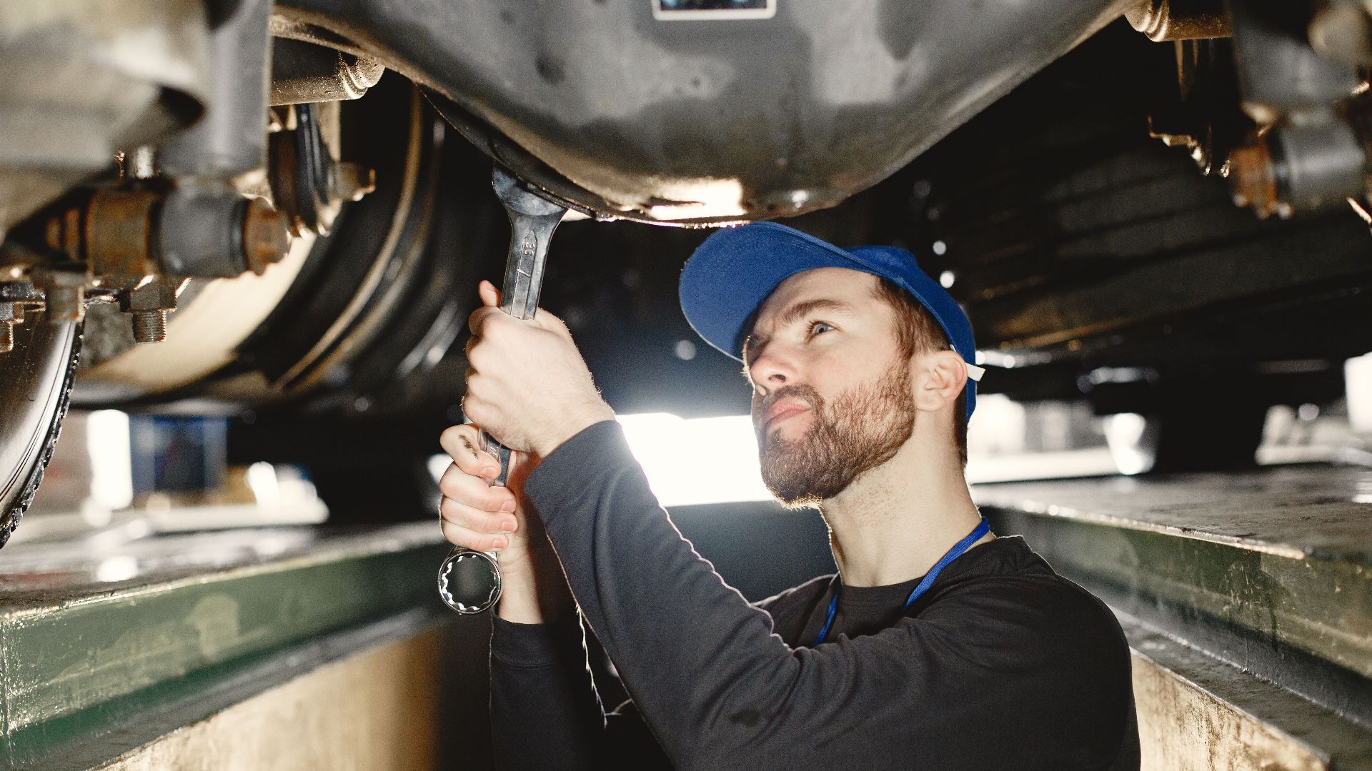 Auto mechanic repairing undercarriage in workshop with focused expression.