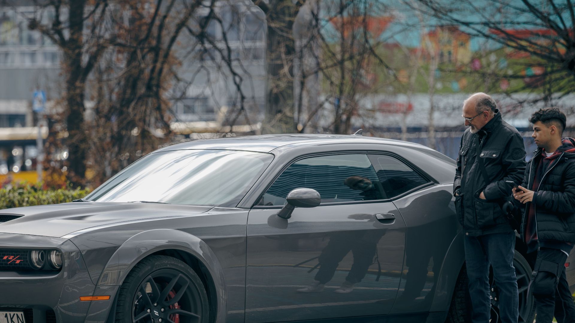A sleek Dodge Challenger R/T is parked outdoors, captured in a bustling urban environment with two people nearby.
