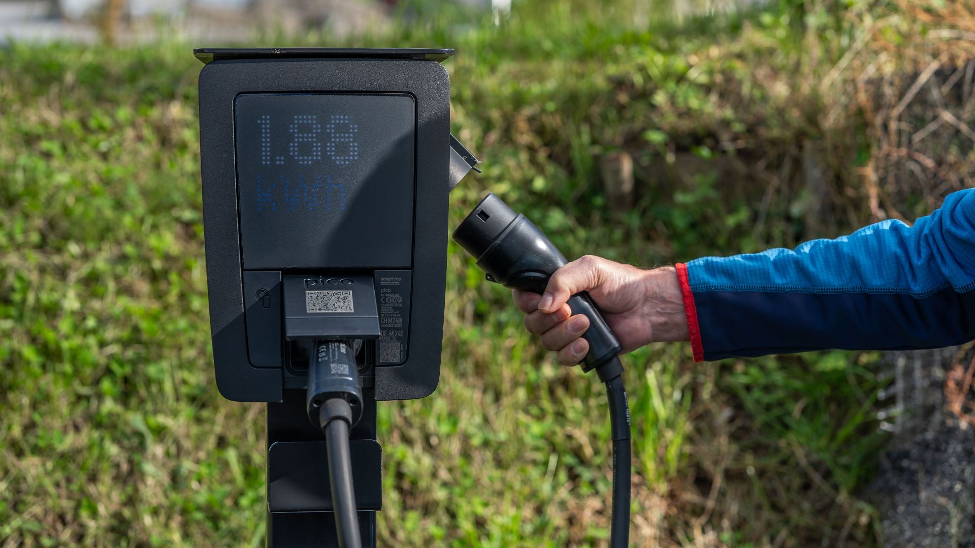 An outdoor electric car charging station with a hand holding a charging cable.