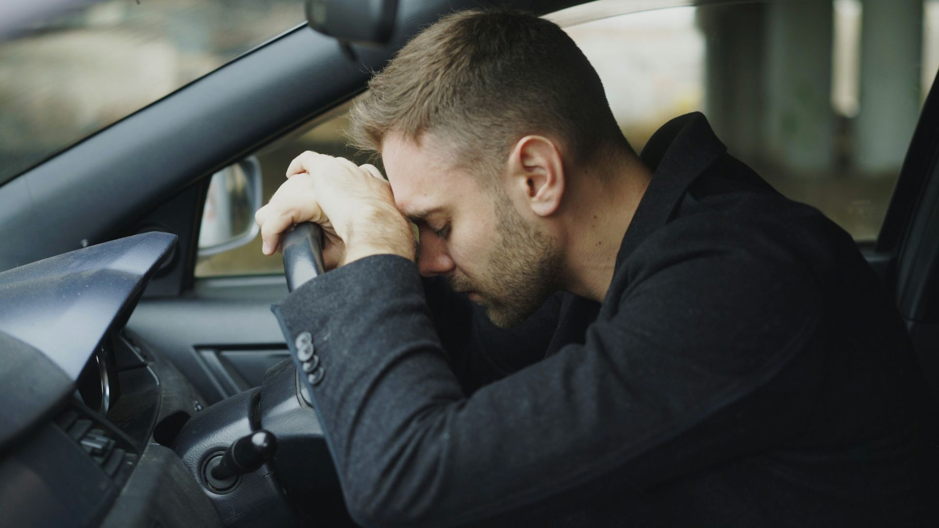 Man resting head on steering wheel in car