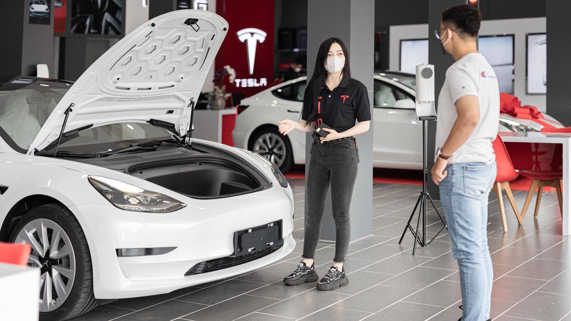 A customer talks with a sales representative about a Tesla Model 3 in a car dealership, showcasing the electric car's features.
