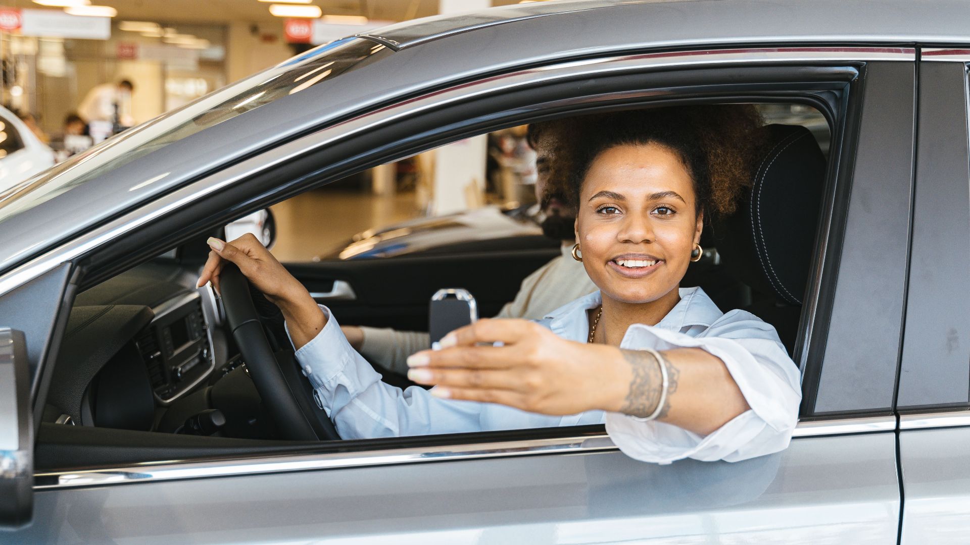 Smiling woman sitting in her new car holding keys, celebrating purchase.