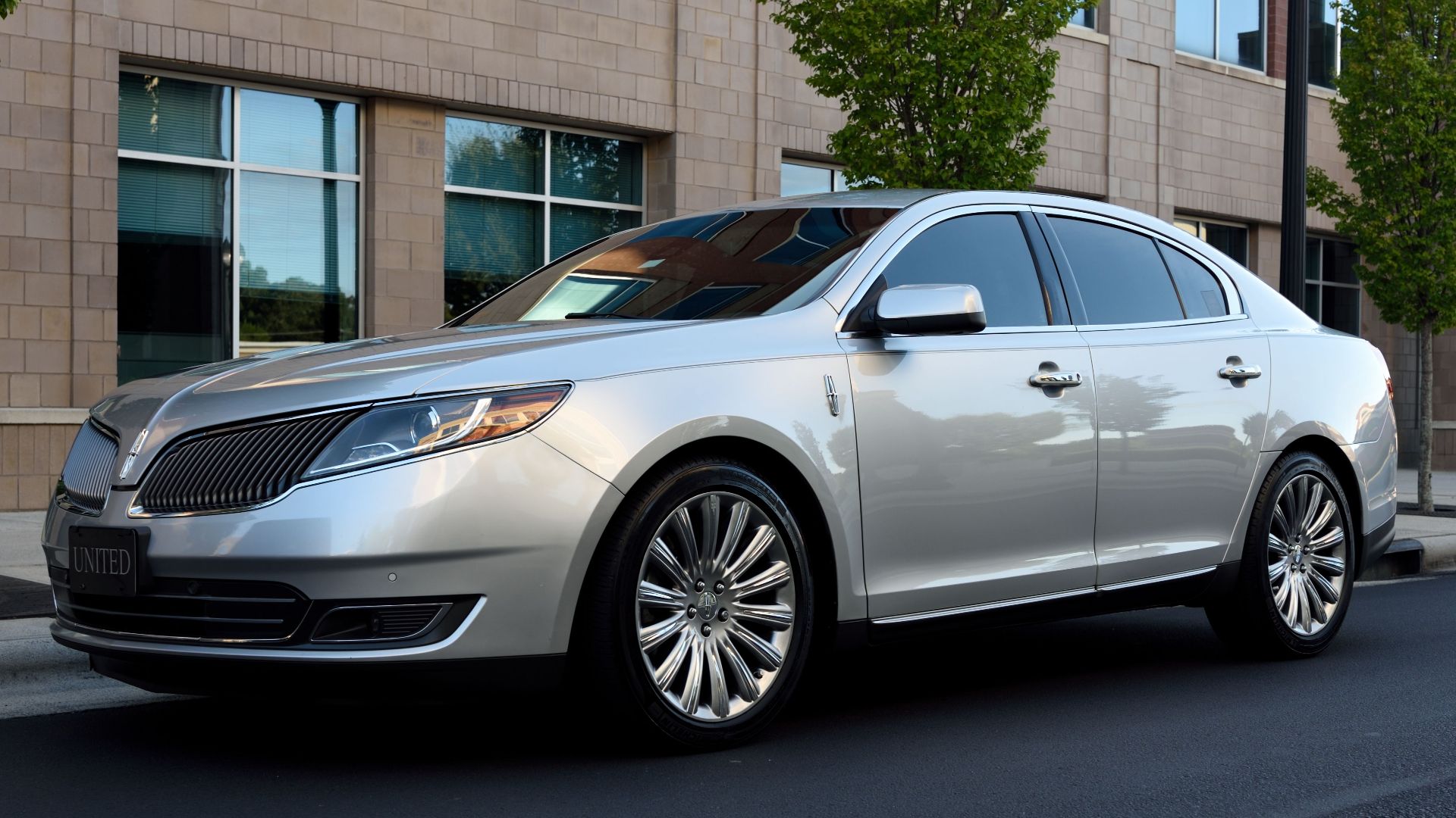 Silver luxury sedan parked beside a modern urban building exterior during the day.