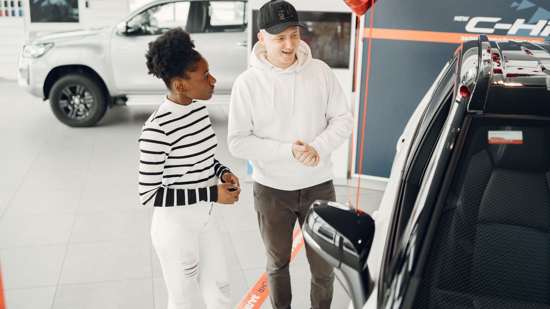 A young couple examines cars in a modern dealership showroom, highlighting customer experience.