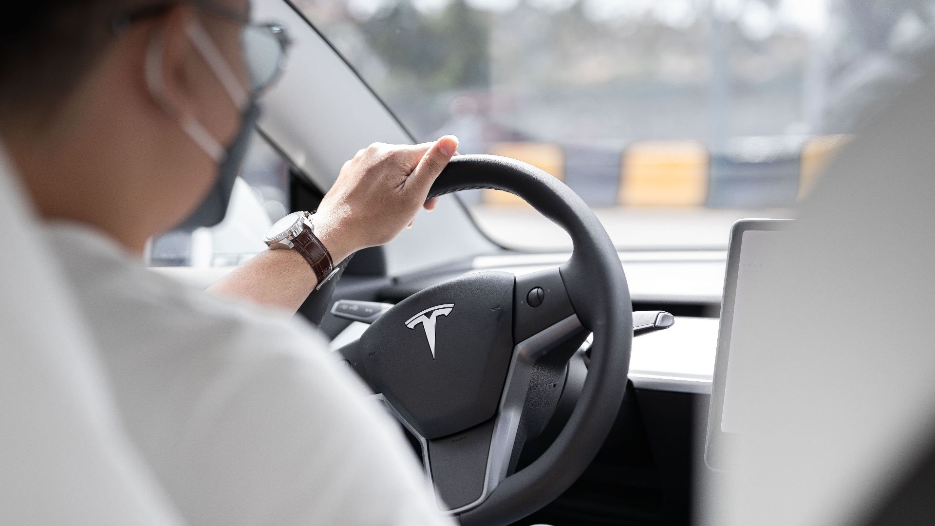 Close-up photo of a person driving a Tesla, showcasing modern vehicle interior design.