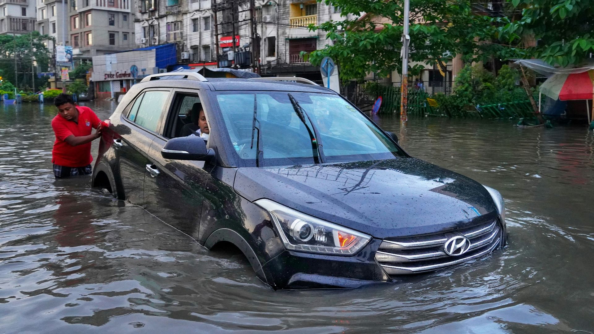 a couple of people standing next to a car in a flooded street