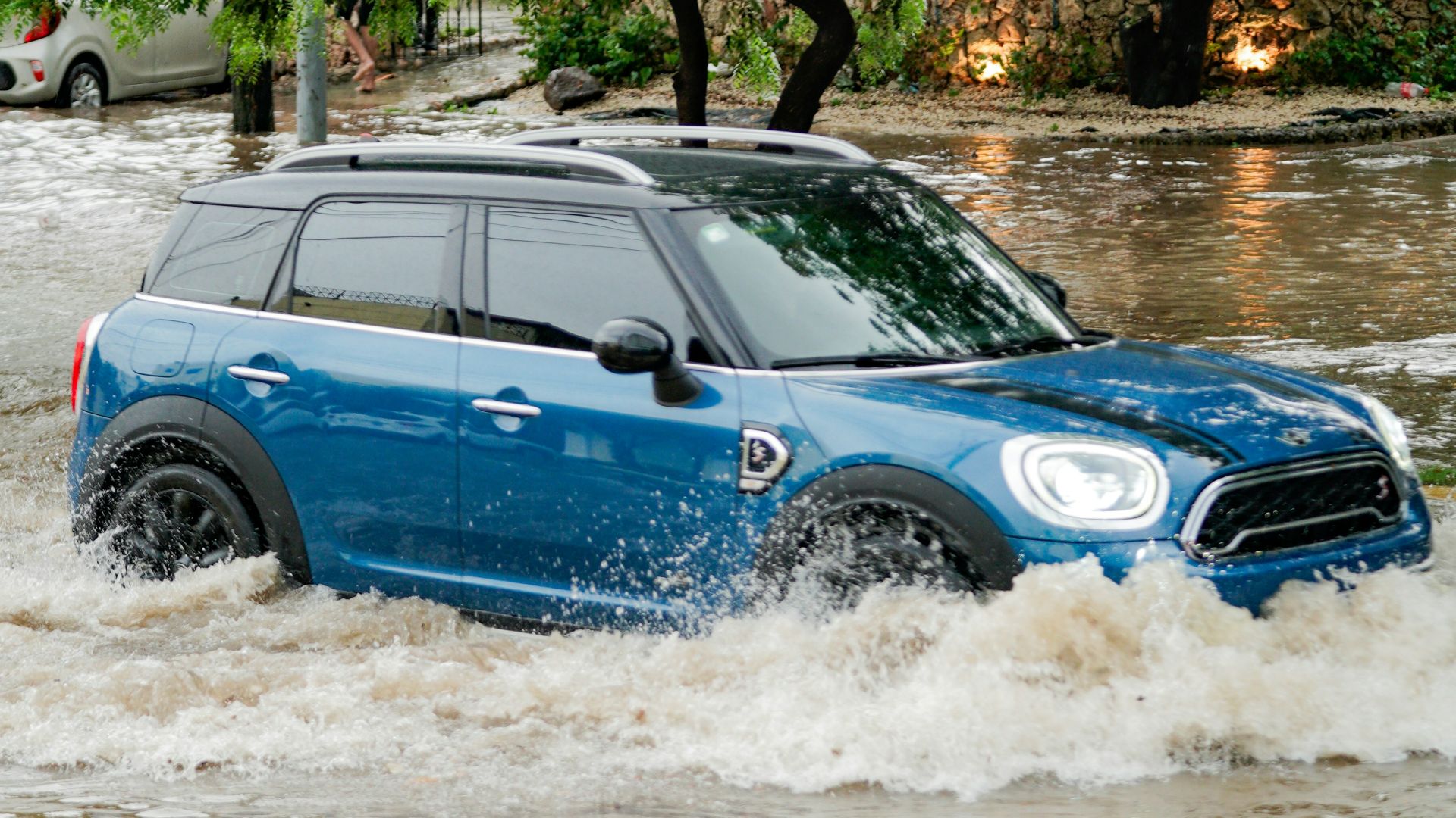 A blue car driving through a flooded street
