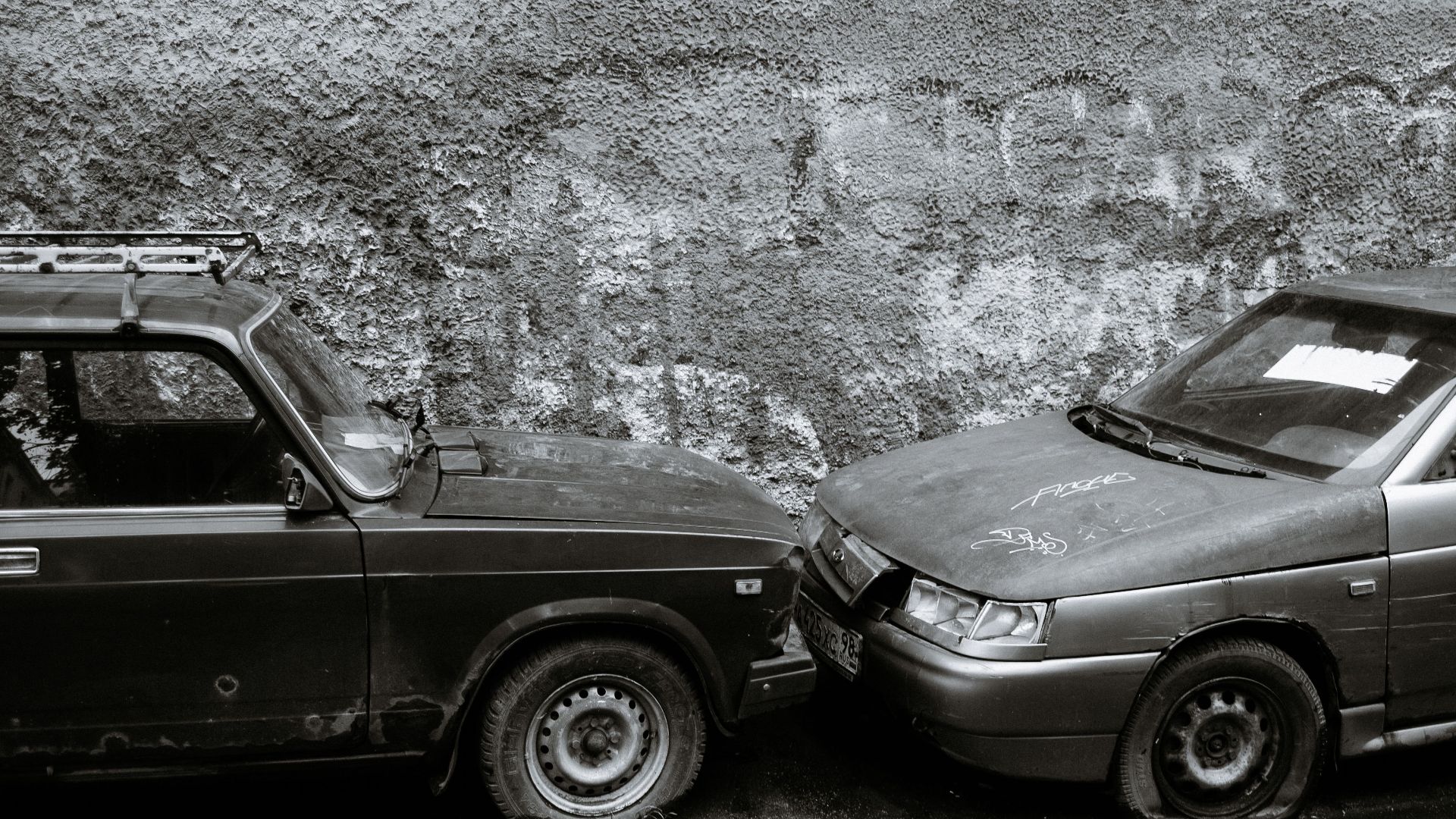 Black and white of aged automobiles with deflated tires near gray wall on street