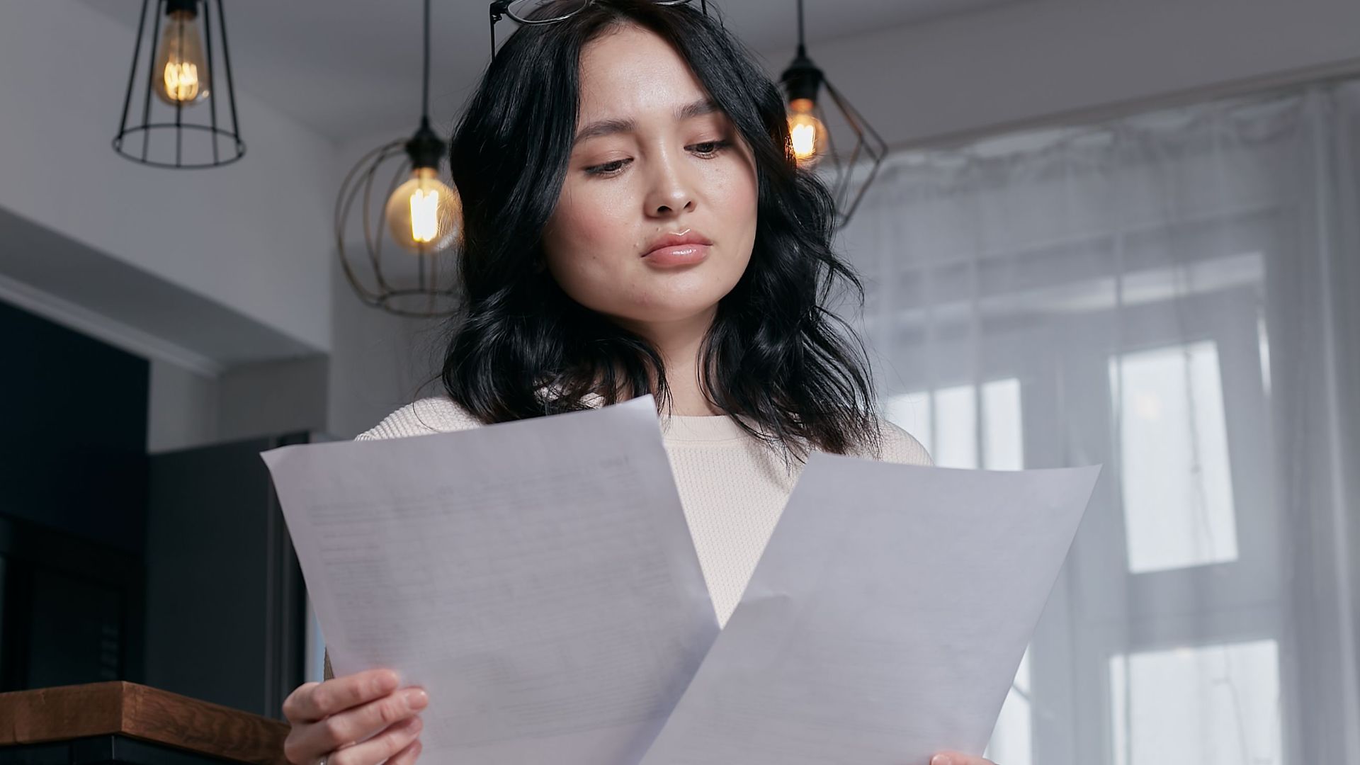A woman sitting indoors, carefully reviewing papers under a stylish lighting setup.