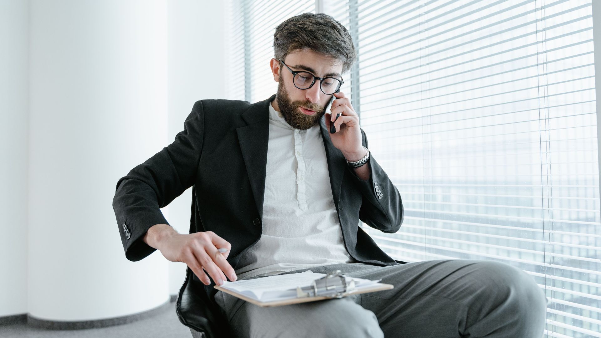 Professional man in office attire, multitasking on phone call and paperwork.