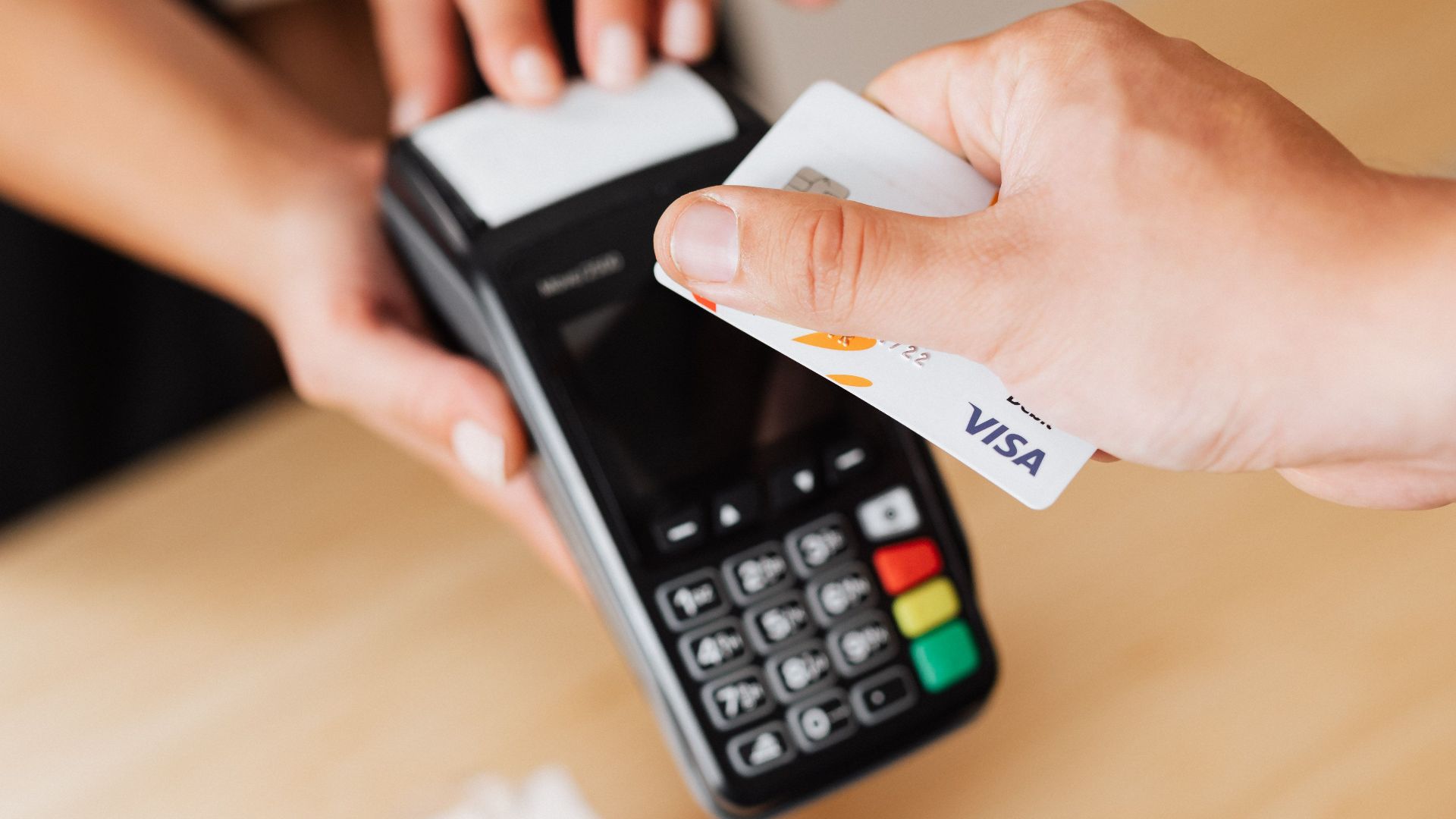 Close-up of hands using a contactless payment terminal with a credit card indoors.