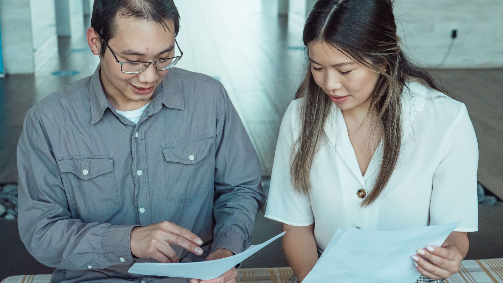 Two coworkers reviewing documents in a modern office, focused on teamwork and planning.
