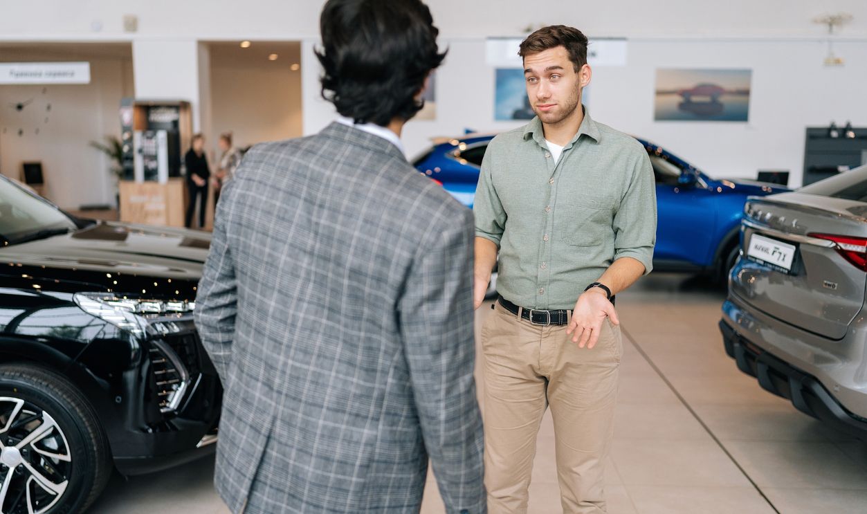 Shutterstock-2367290263, Ufa, Russia - 22 June 2023. Rear view of unrecognizable professional male car seller with serious male customer in auto dealership, talking about specifications and performances of vehicle. Customers
