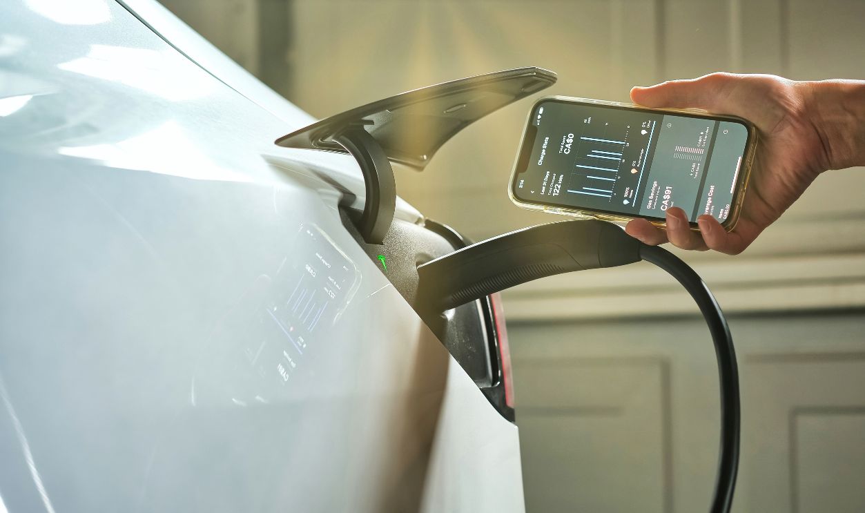 Toronto, Ontario, Canada - May 1, 2022 :  Man showing Tesla mobile app on smartphone while charging Model Y at home. Clearly EV car saved lots of money cost for family comparing with spending on gas. 