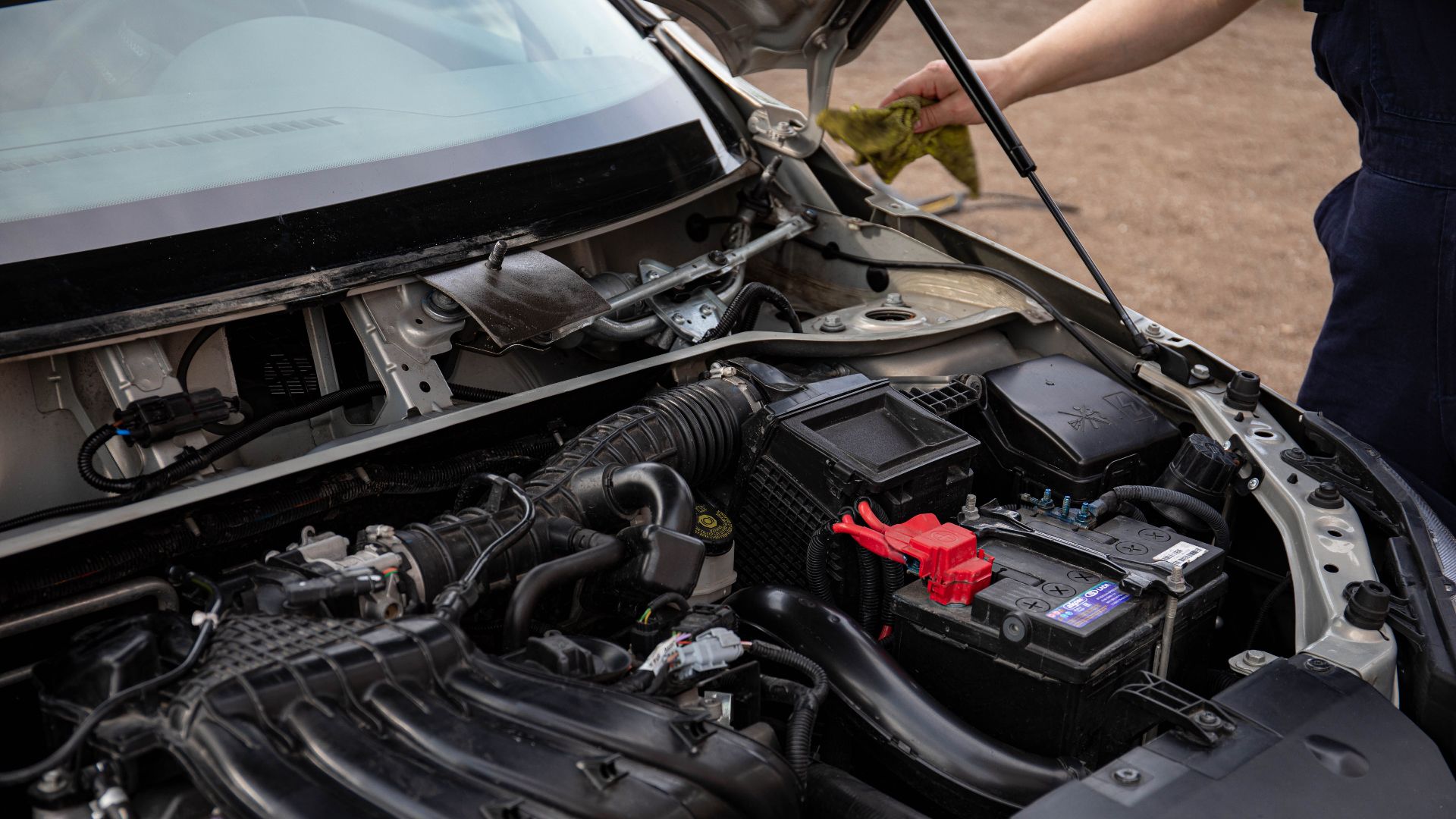 Mechanic inspecting car engine bay and battery during routine maintenance.