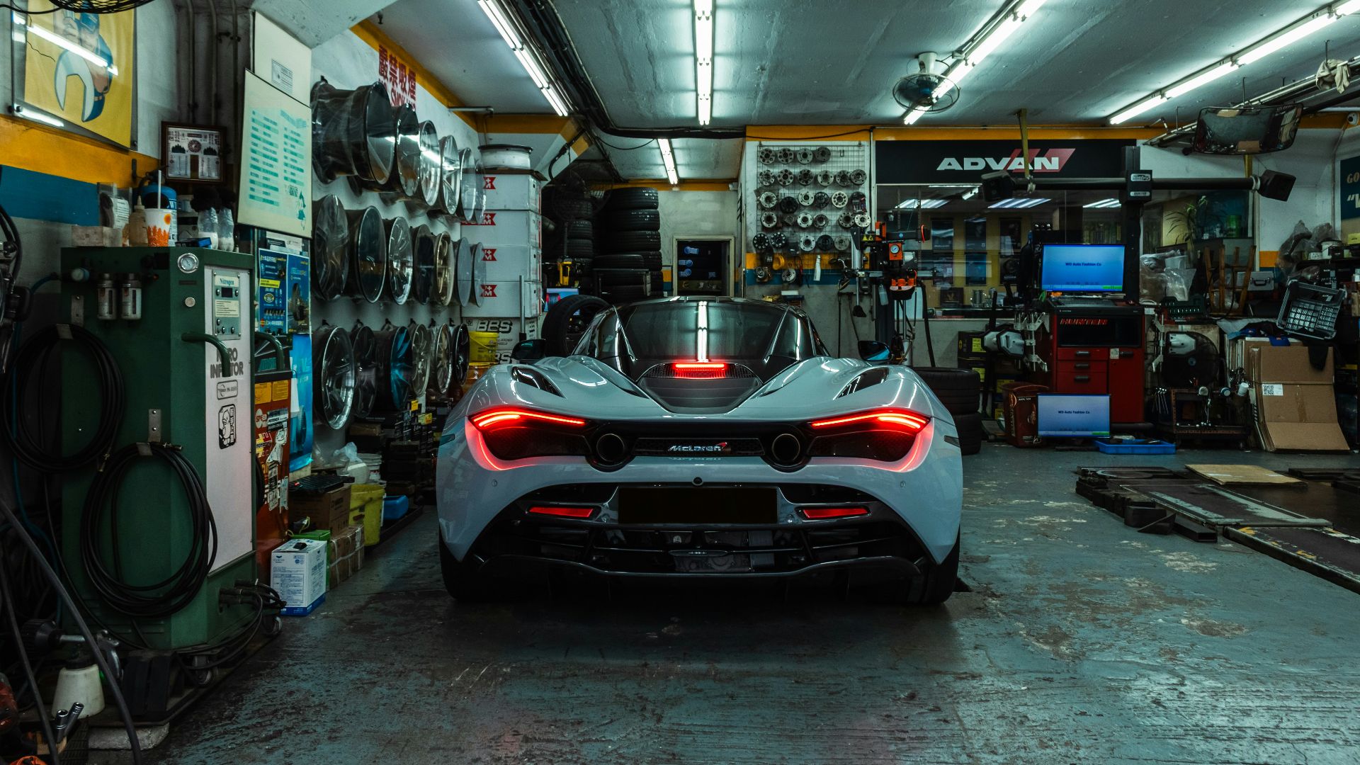 A light blue sports car with glowing red taillights inside an automotive repair shop