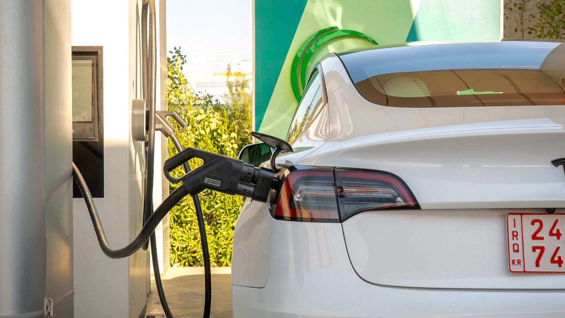 Tesla Model 3 electric vehicle charging at a station outdoors during the day.