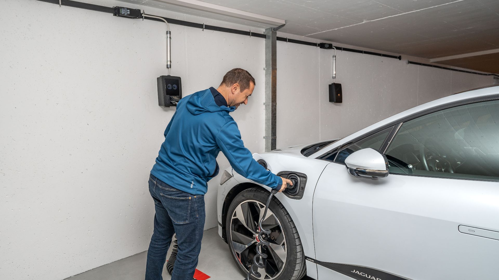 A man connects an electric car to a charging station in a modern indoor garage setting.