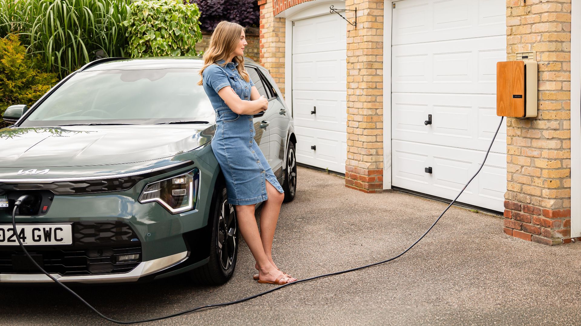 Woman charging electric vehicle at home with a modern wall-mounted charging station.