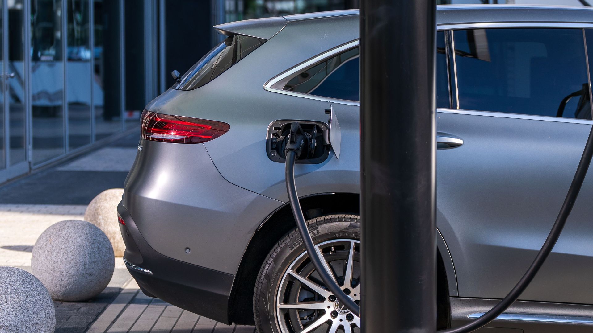 A silver electric car charging at an urban station, highlighting sustainable living in a modern cityscape.