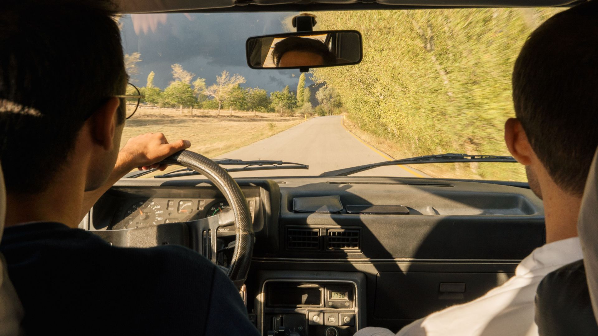 Two adults driving through scenic countryside near Merzifon, Türkiye, in a vintage car.