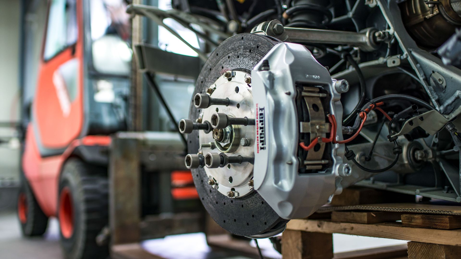 Detailed view of an automotive brake caliper and disc in an industrial workshop setting.