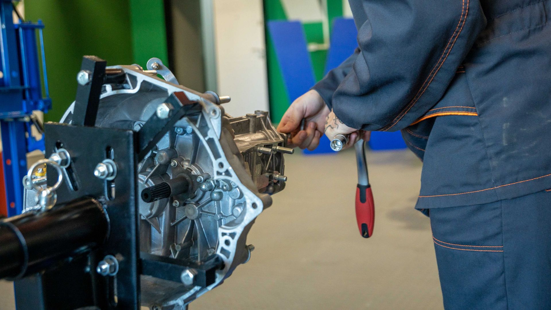 Mechanic uses tools to repair car transmission in an indoor workshop setting.