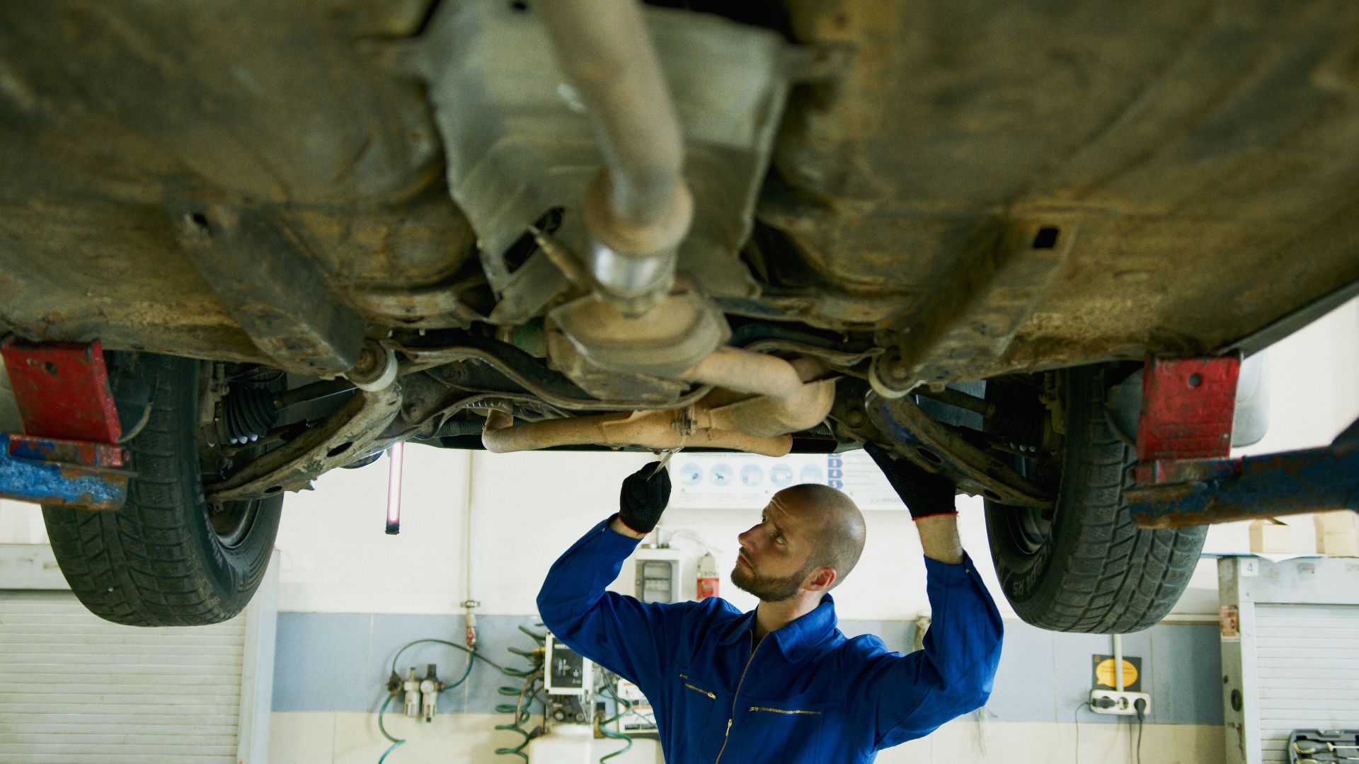 Mechanic examining the underside of a car in an auto repair shop for maintenance.