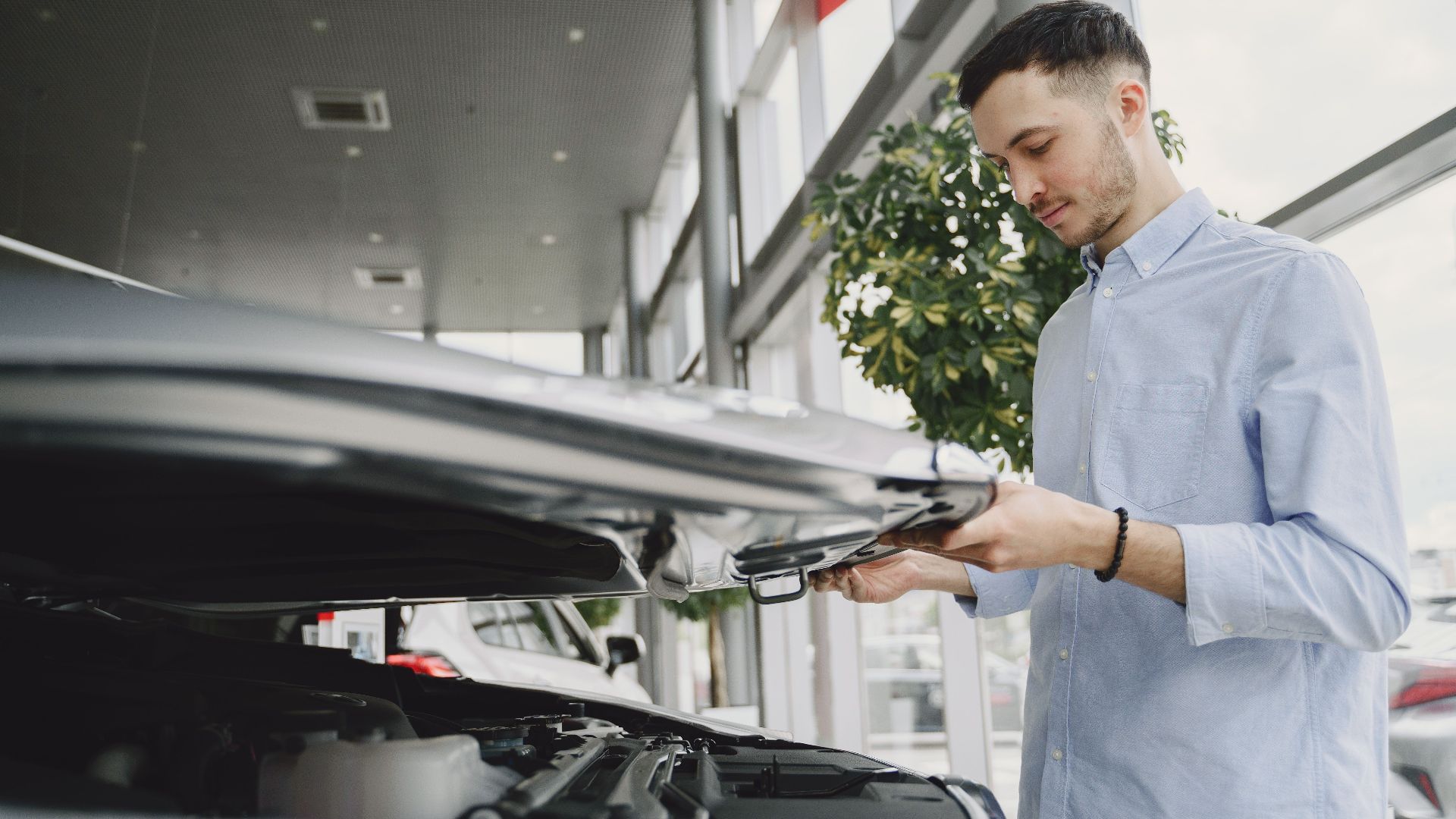Young man checking car engine in modern dealership showroom.