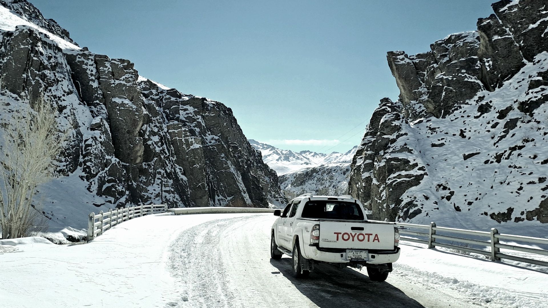 A serene winter drive through Behsud, Wardak with snow-covered mountains and a white car.