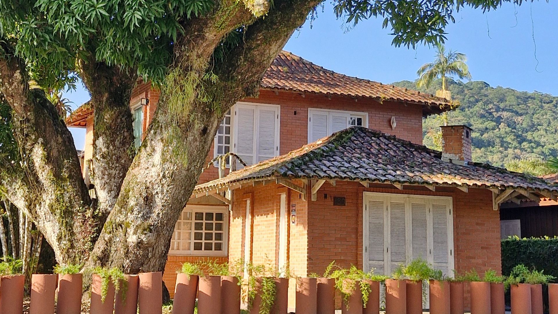 A picturesque brick house surrounded by verdant trees under a clear blue sky.