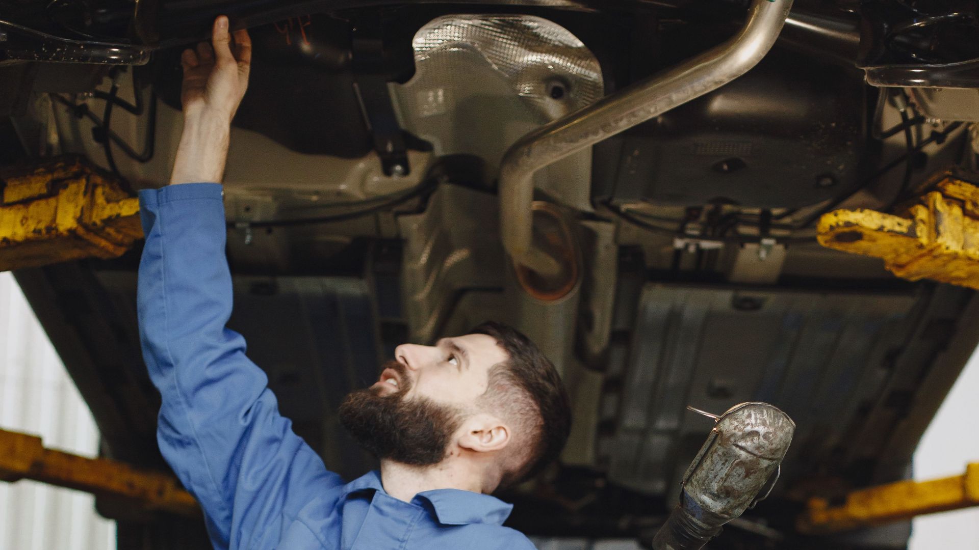 Mechanic in workwear inspecting vehicle underside in a garage environment. Service and maintenance concept.