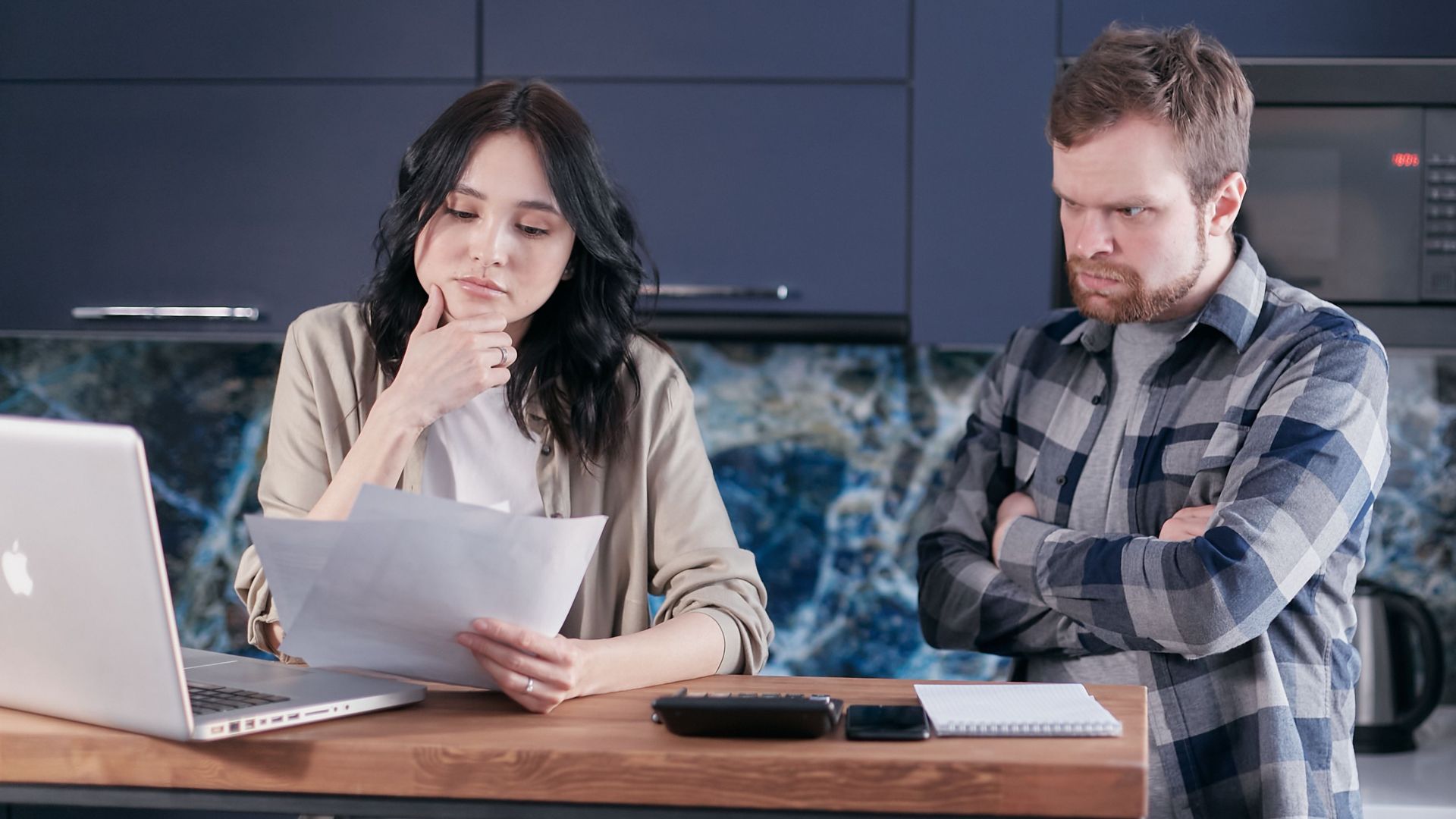 A couple sitting at a kitchen desk reviewing financial documents, using a laptop.