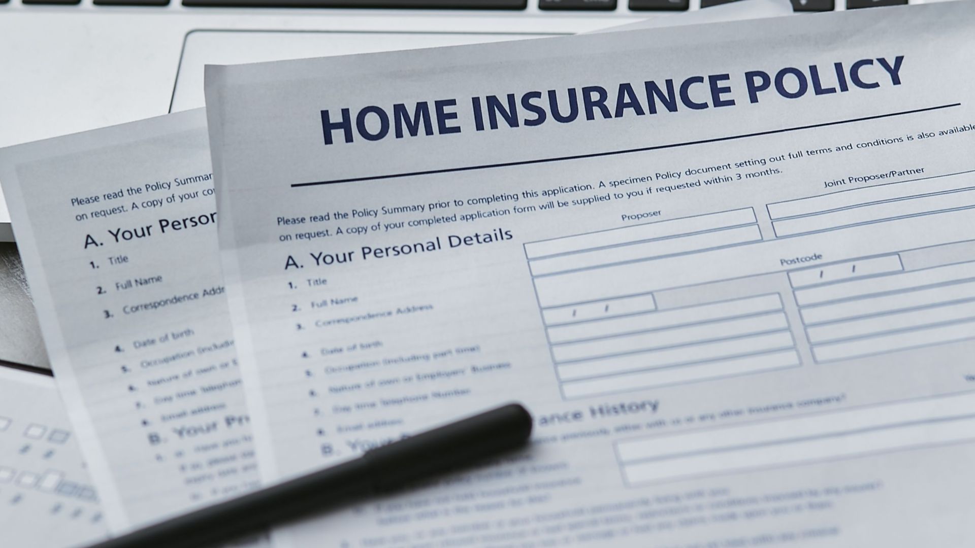 Close-up of home insurance documents with a laptop, symbolizing modern paperwork processes.
