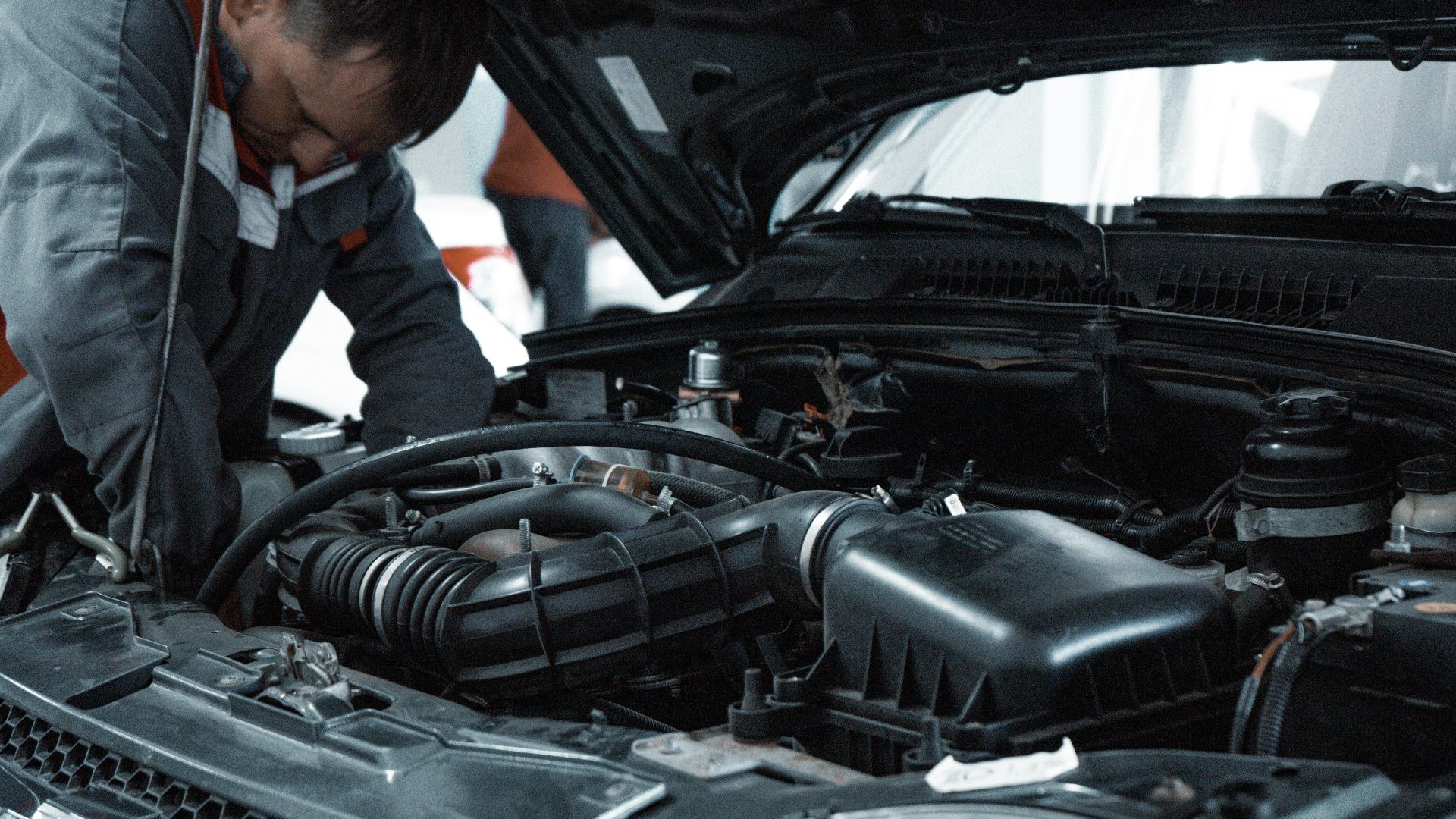 A mechanic in a grey uniform inspecting the engine of a car