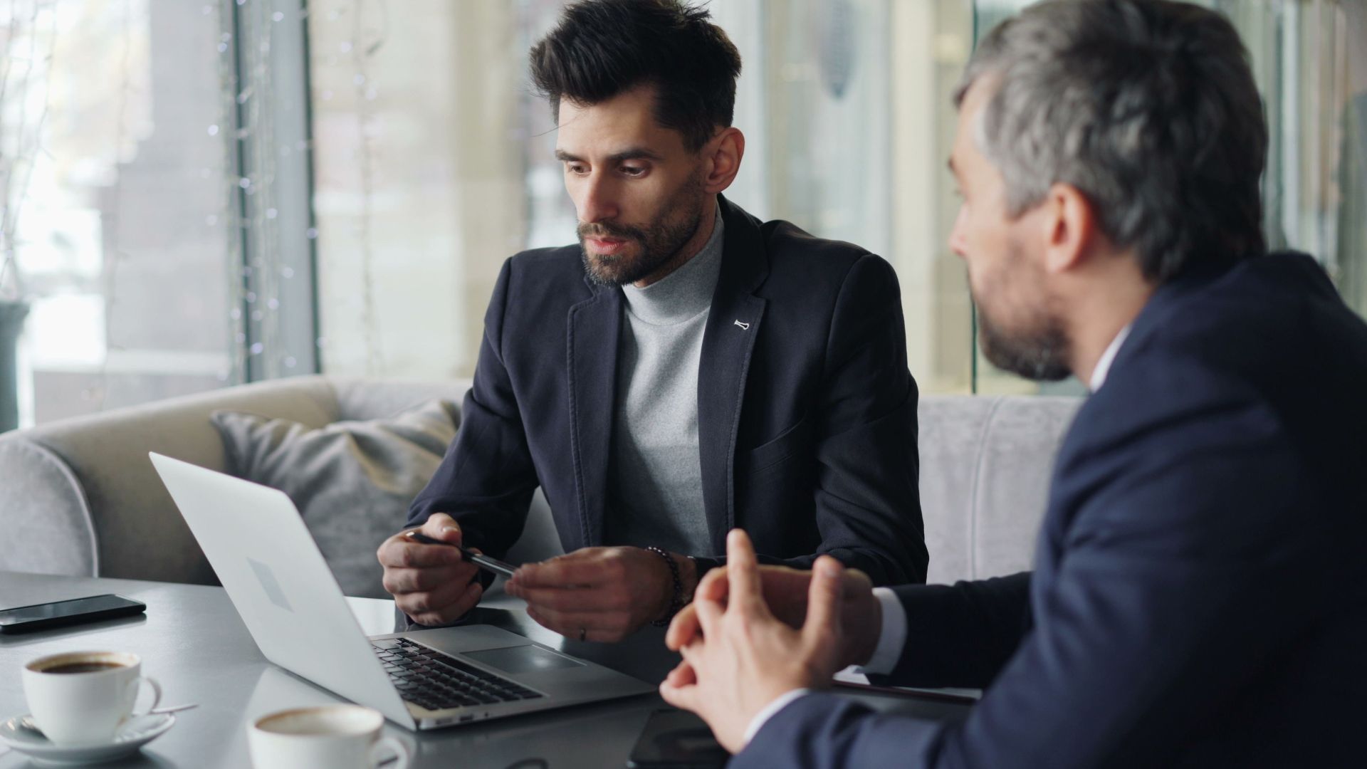 Two businessmen engaged in a meeting in a cozy café, discussing on a laptop.