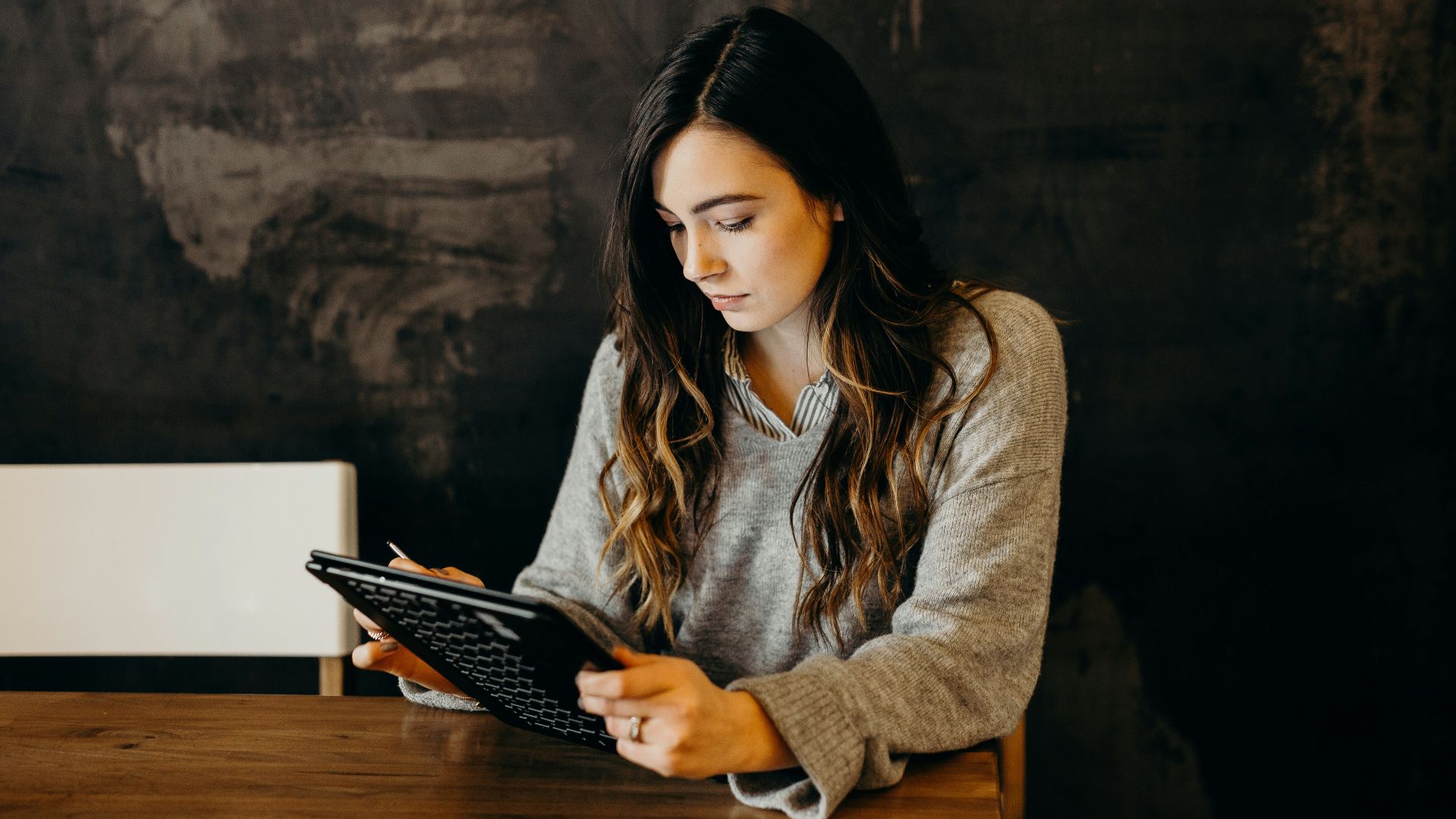 A woman in a grey sweater using a tablet at a wooden table