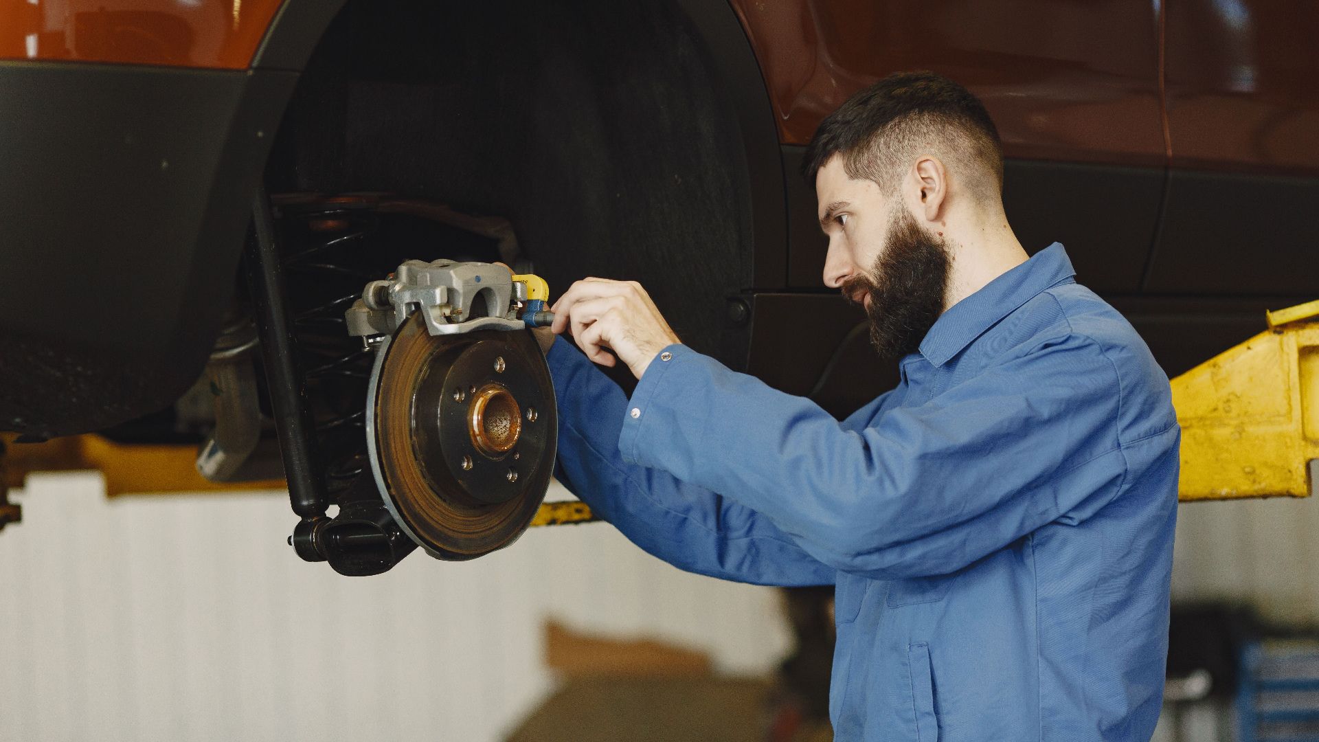 Mechanic in blue uniform performing brake repair on car in modern garage.