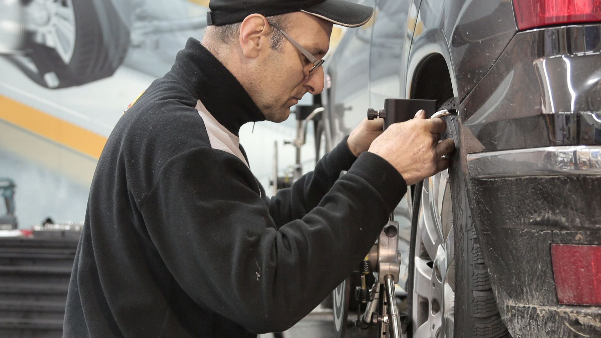 Side view of a mechanic aligning a car tire in a professional auto workshop.