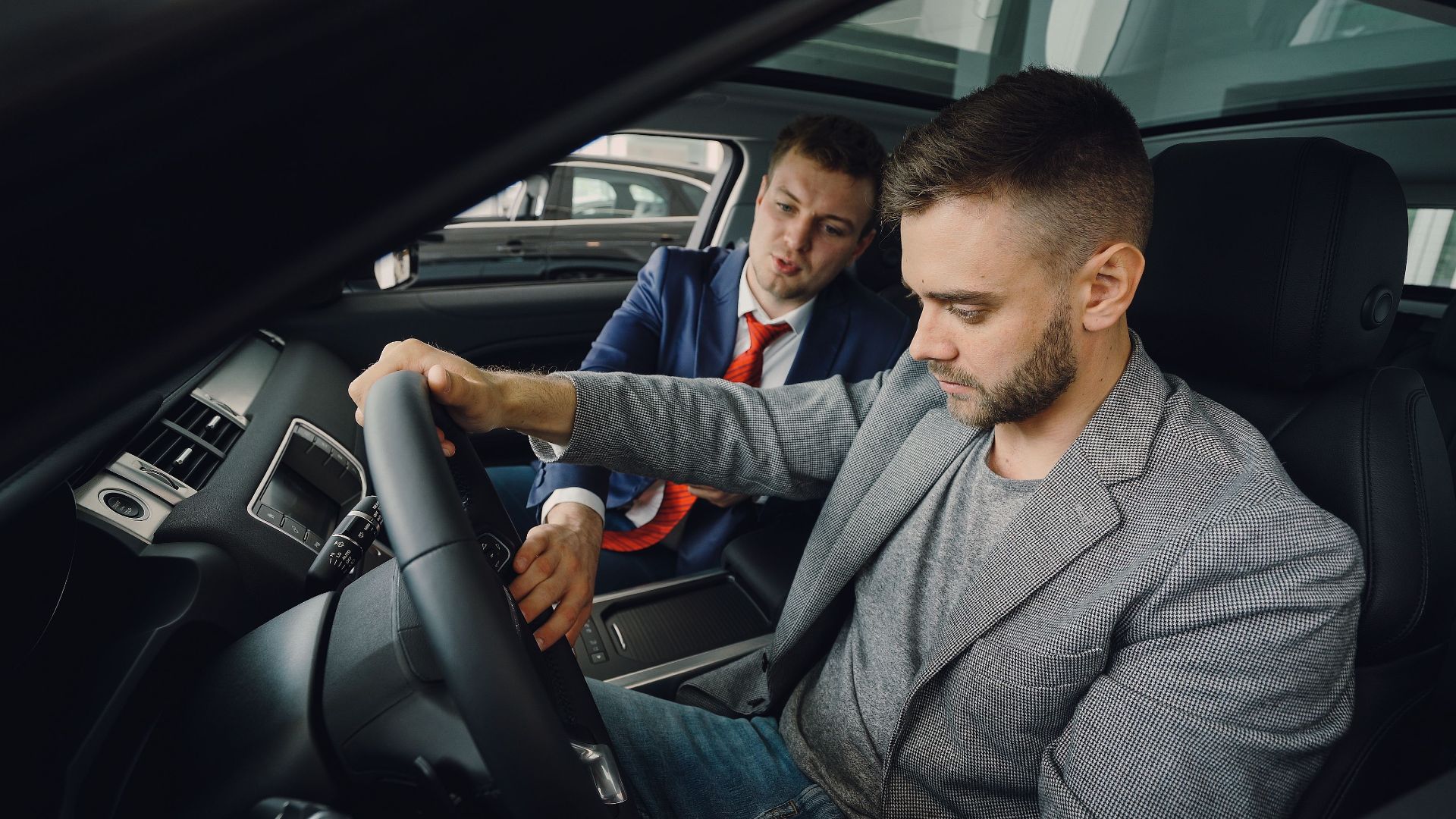 Salesman demonstrating car features to potential buyer inside vehicle showroom.