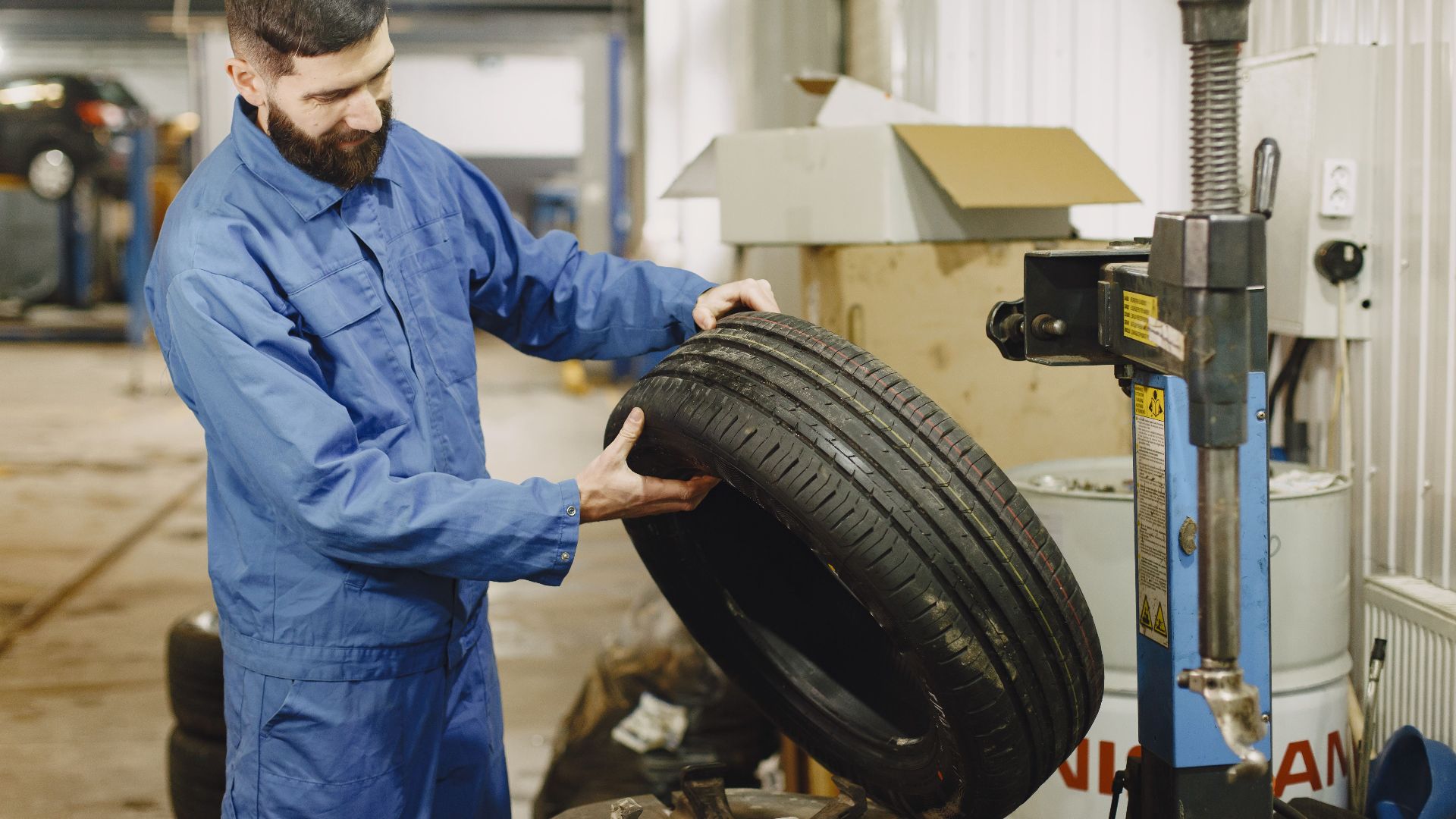 Mechanic in blue uniform examining a tire in an automotive garage.