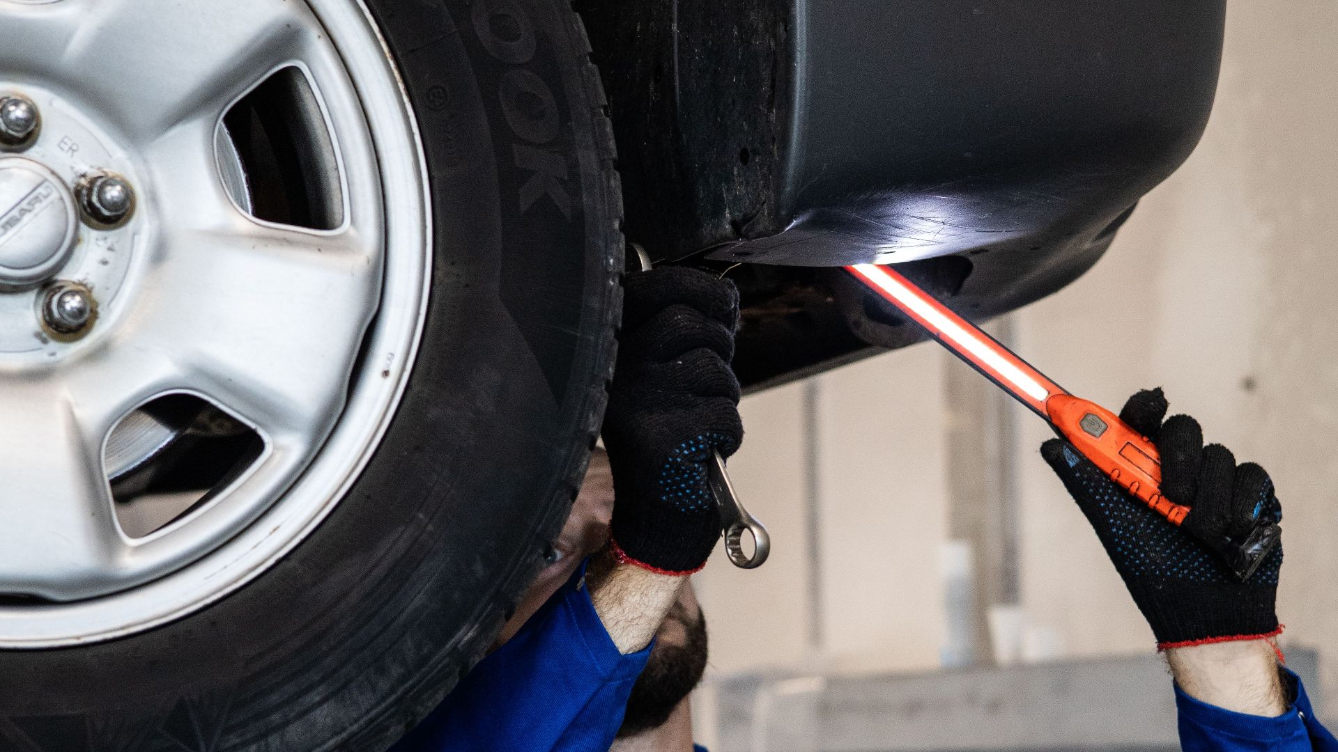 Mechanic inspecting a car in an auto repair shop, checking under the vehicle with a flashlight.