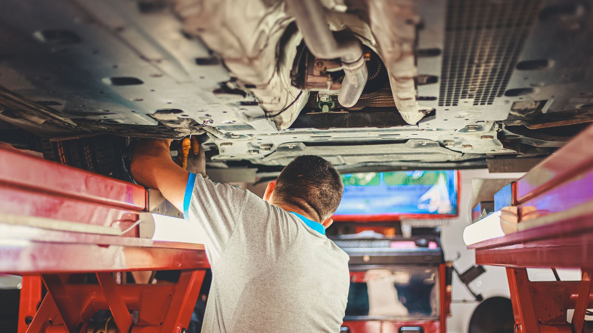 A mechanic works under a lifted car in an auto repair shop, adjusting parts.