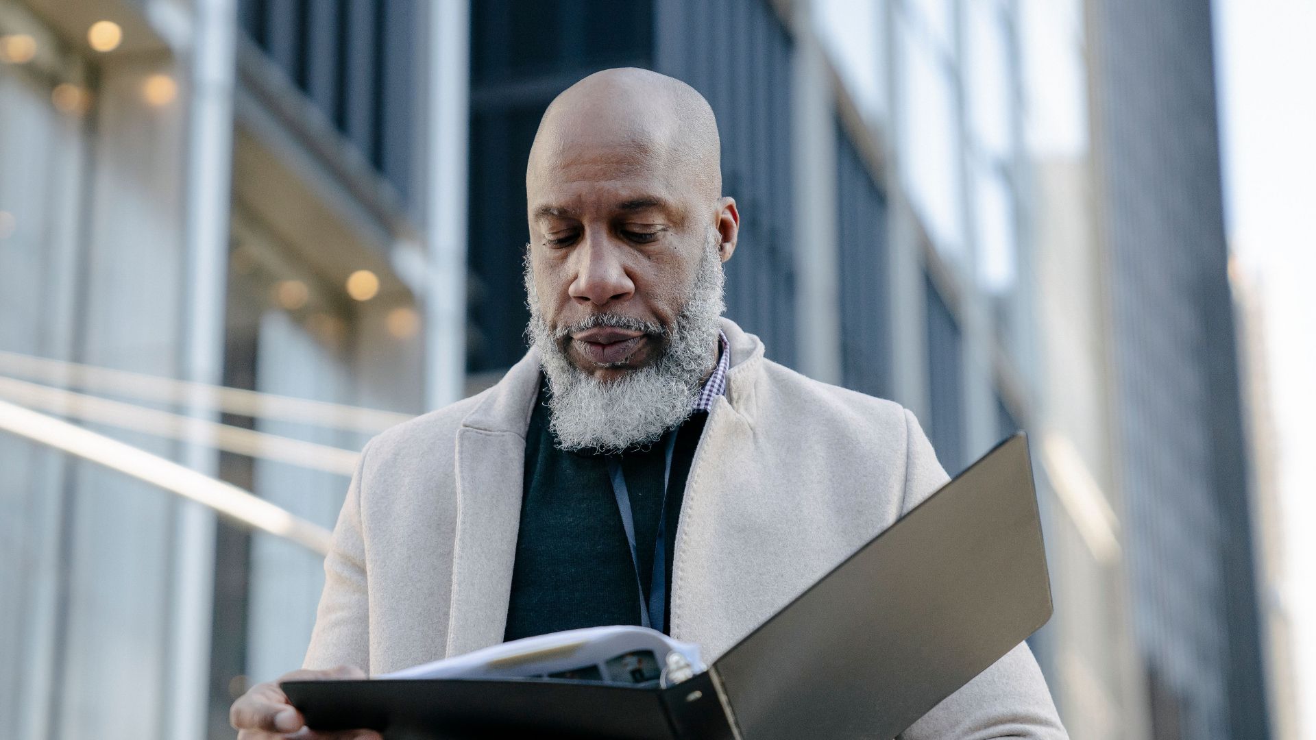 African American man reading a book outside modern office buildings in a city setting.