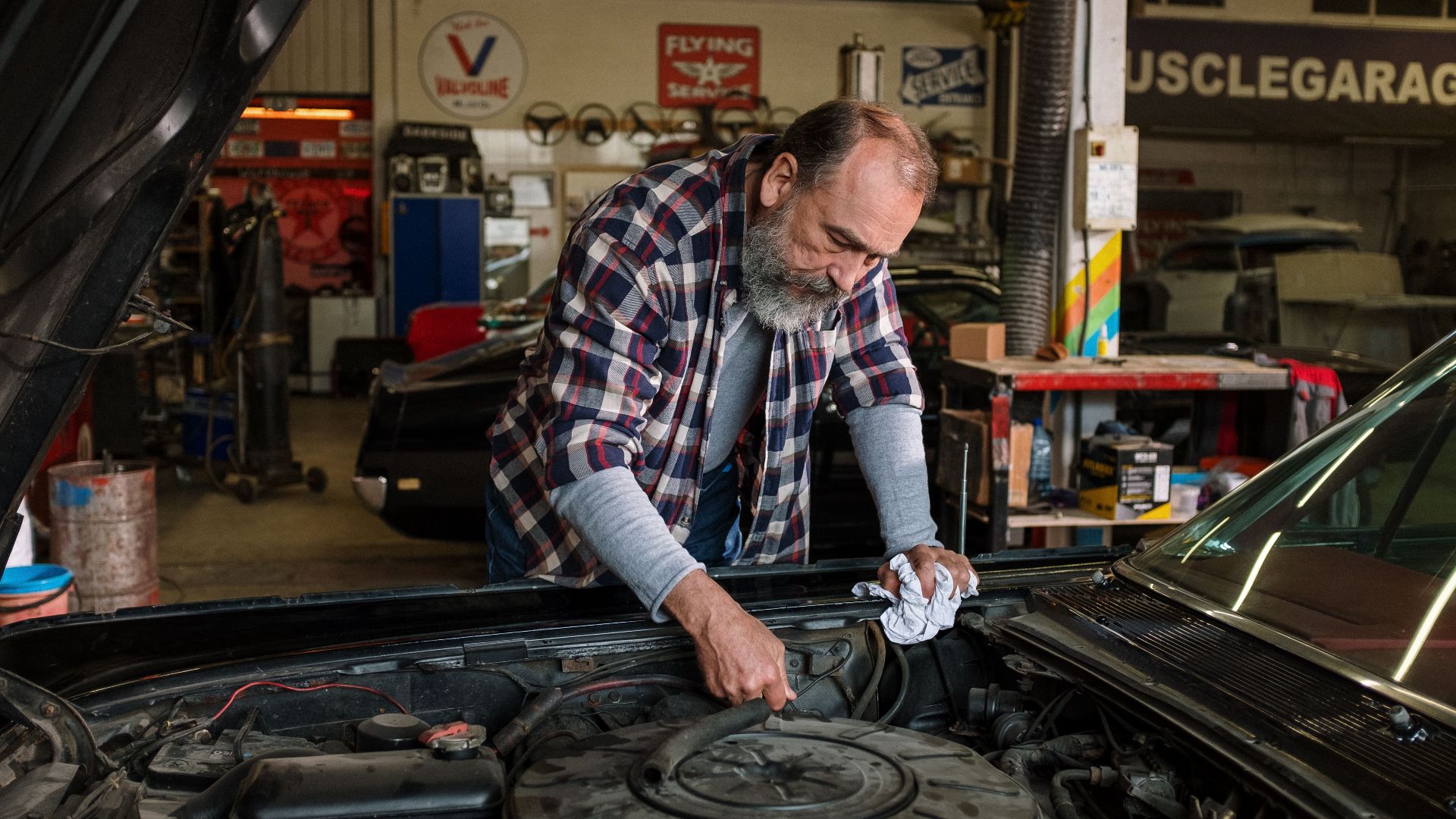 Bearded mechanic working on engine repair in an auto repair shop garage with a focus on hands-on car service.