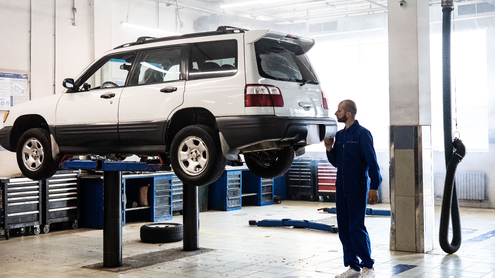 Mechanic inspecting a lifted SUV in a modern auto repair garage.
