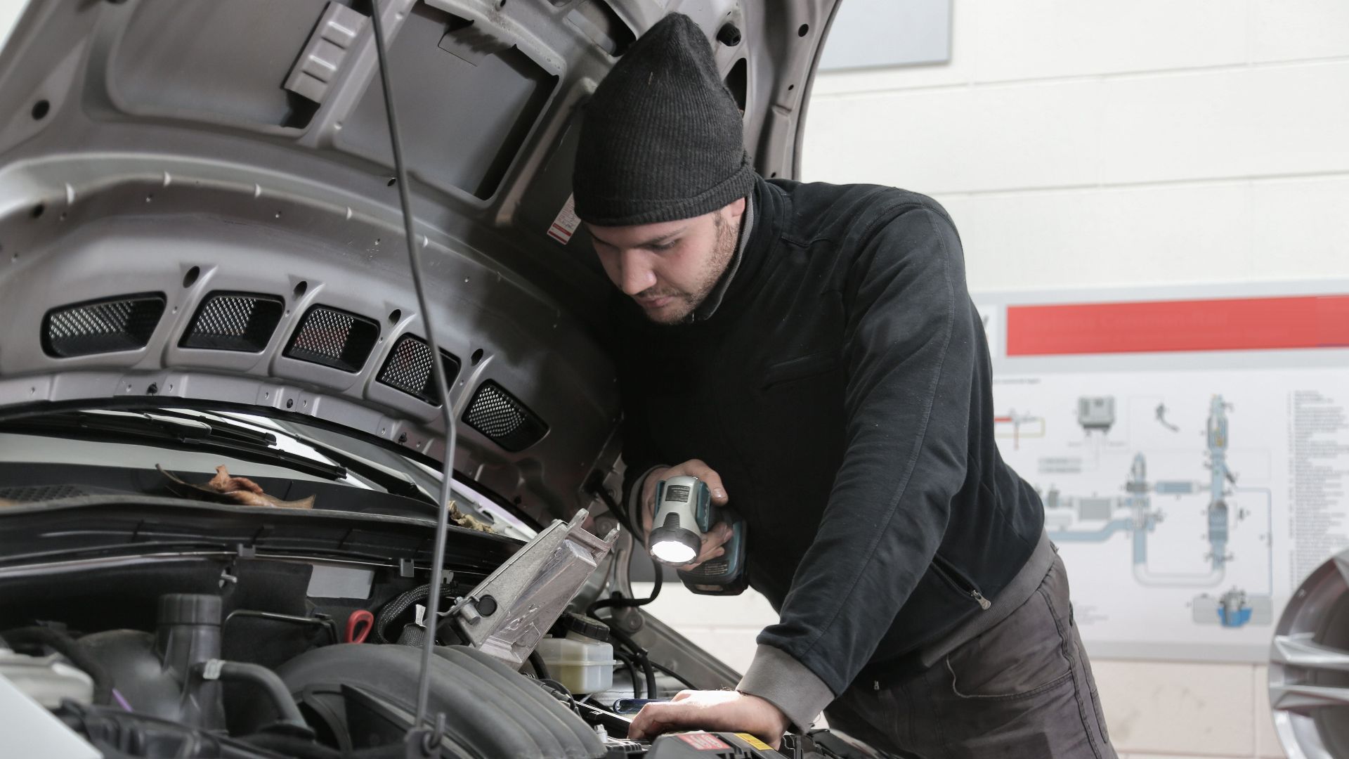A mechanic closely inspects a car engine in a garage using a flashlight, ensuring proper maintenance.