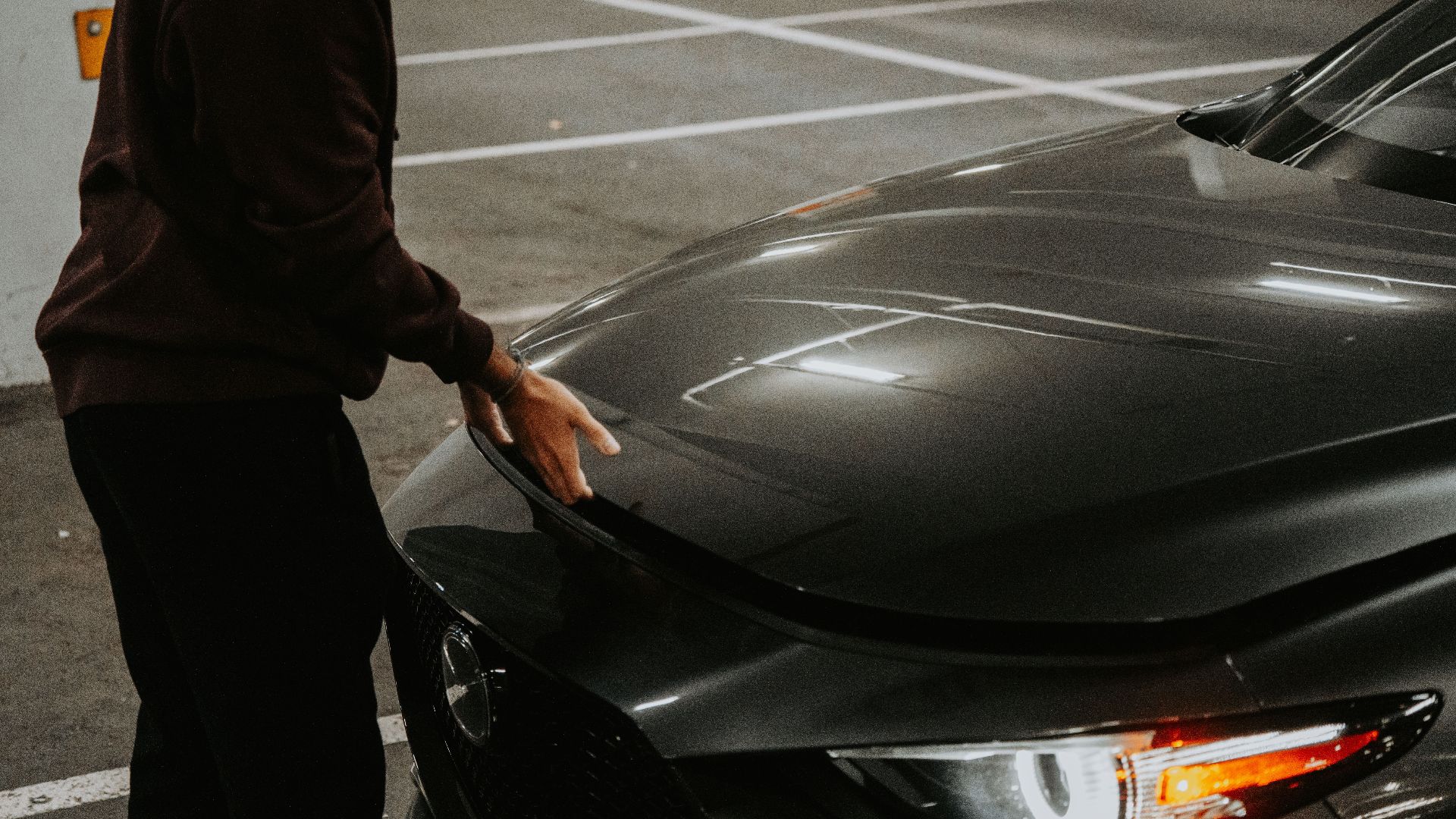 A person opens the car hood in a dimly lit parking garage, showcasing urban transportation.